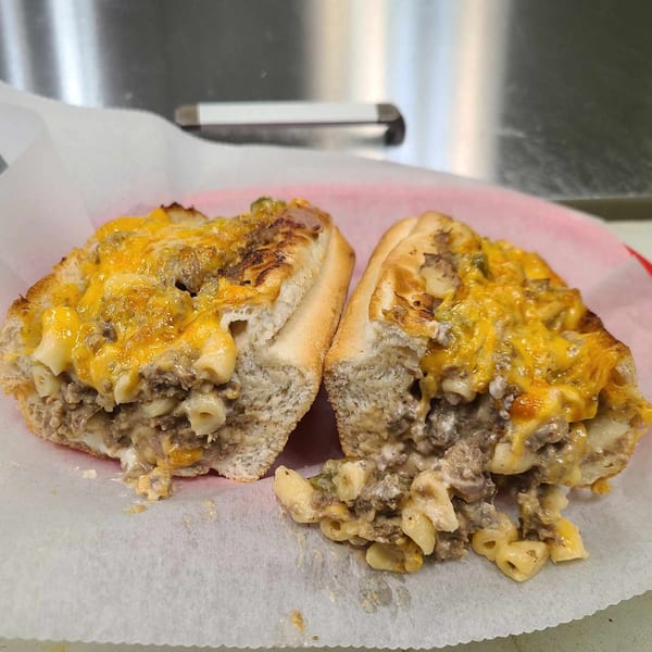 A Mash Hoagies cheesesteak hoagie, cut in half, filled with ground meat, macaroni, and melted cheese.