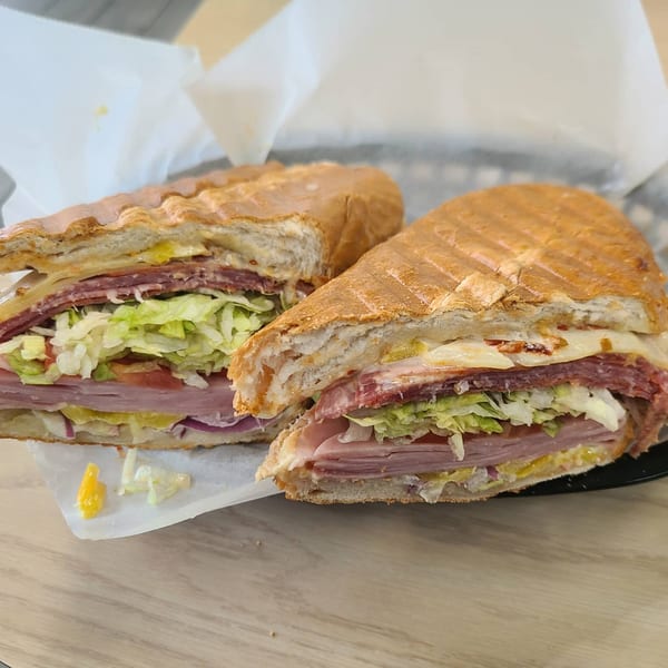 A Mash Hoagies sandwich, cut in half, revealing layers of meat, cheese, lettuce, and tomato.