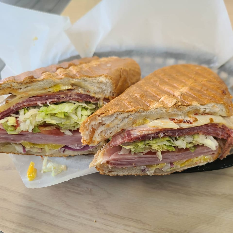 A Mash Hoagies sandwich, cut in half, revealing layers of meat, cheese, lettuce, and tomato.