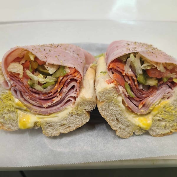 A Mash Hoagies Italian hoagie, cut in half, with ham, salami, lettuce, tomato, and pickles.