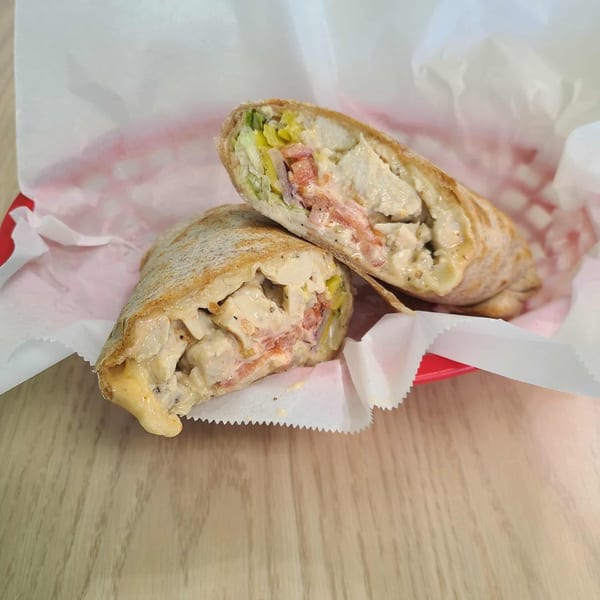 Two halves of a Mash Hoagies chicken wrap, filled with creamy sauce, tomatoes, and peppers.