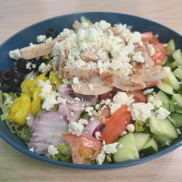 A vibrant salad with grilled chicken, feta, olives, peppers, tomatoes, cucumbers, and red onion.