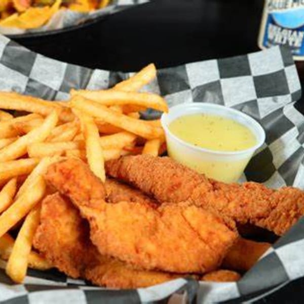 Chicken tenders and fries with a side of dipping sauce in a checkered paper-lined basket.