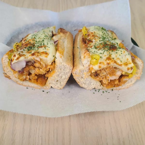 A Mash Hoagies hoagie, cut in half, filled with meat, cheese, and peppers, on white paper.