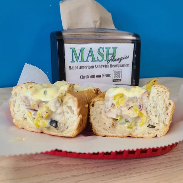 Two halves of a Mash Hoagies sandwich filled with creamy chicken salad, peppers, and onions.