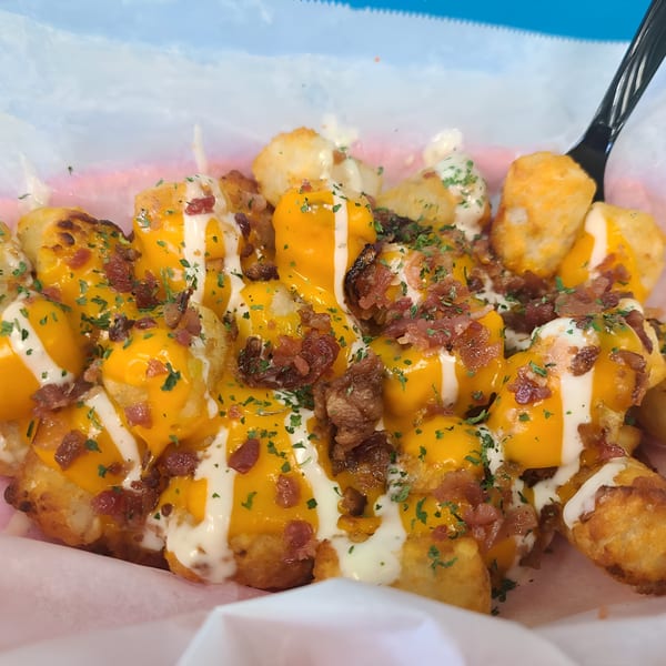 Loaded tater tots with melted cheese, bacon bits, and white sauce, garnished with parsley.
