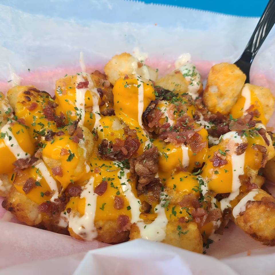 Loaded tater tots with melted cheese, bacon bits, and white sauce, garnished with parsley.
